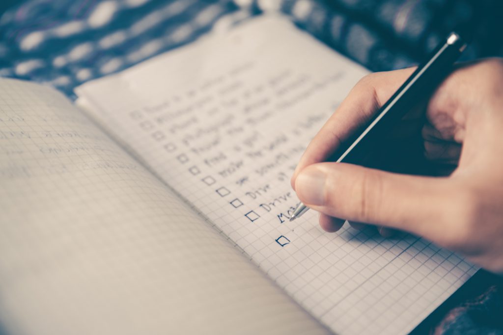Hand schreibt eine Checkliste in ein Notizbuch